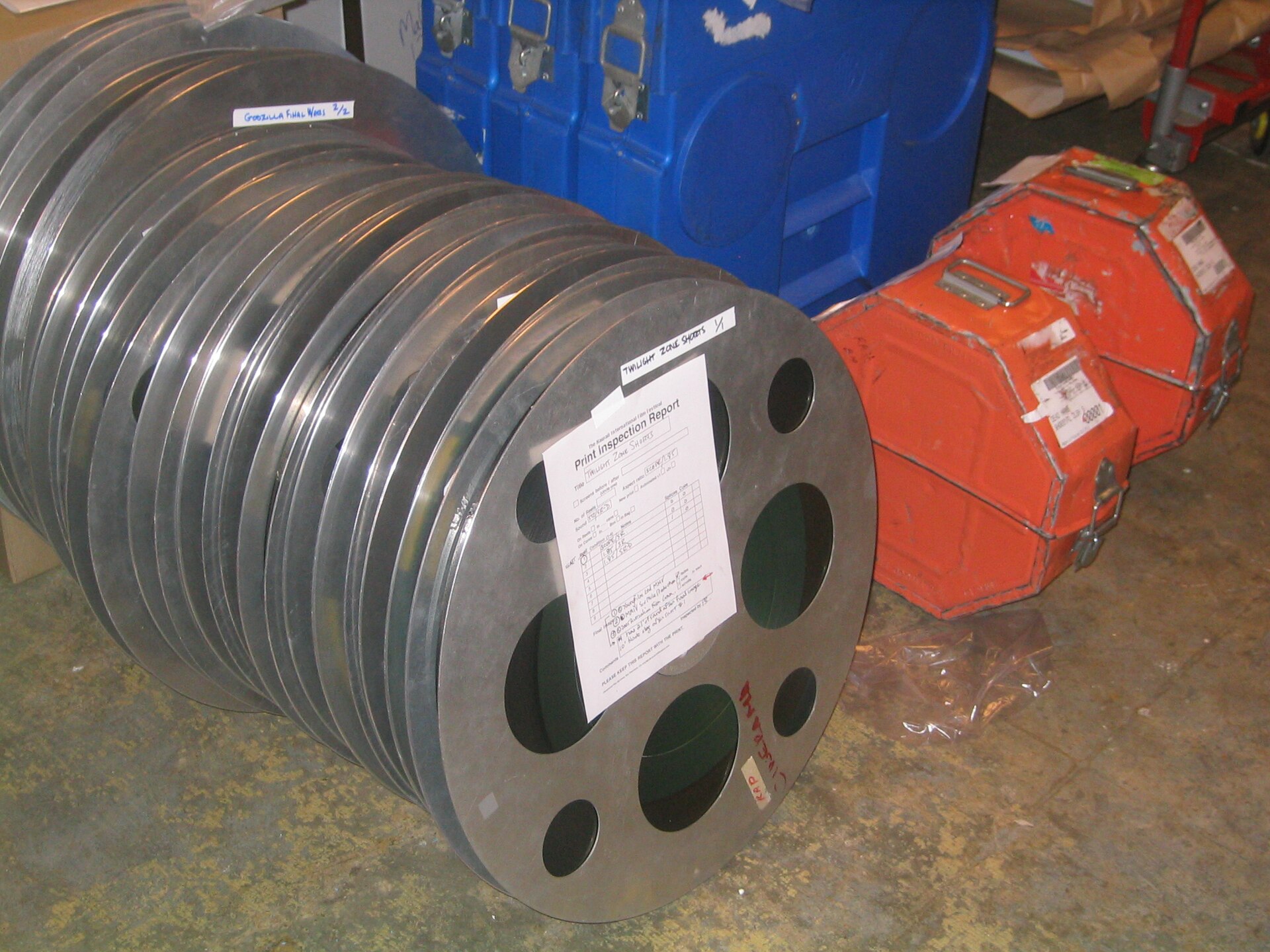 35 मिलीमीटर फ़िल्म के कई रील और उनके धातु के डिब्बे, किसी और फ़िल्म के संग्रह की तस्वीर। पुरस्कृत फ़ीचर फ़िल्म भी उसी शाम ऐसे ही रीलों पर वहाँ चली थी।