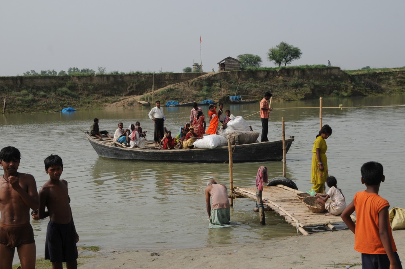 बिहार में बाढ़ के पानी पर लोगों को ले जाती एक देसी नाव और किनारे पर खड़े बच्चे। यह तस्वीर 2008 की बाढ़ की है; कटिहार के प्रतापगंज में स्कूल का रास्ता इन दिनों नाव से तय होता है
