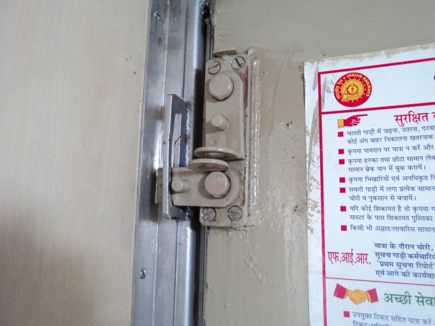 भारतीय रेल के एक आरक्षित डिब्बे के प्रवेश-द्वार की चिटकनी, बगल में रेलवे की सुरक्षित-यात्रा वाली सलाह चिपकी हुई; यह तस्वीर 2011 की और एक वातानुकूलित डिब्बे की है